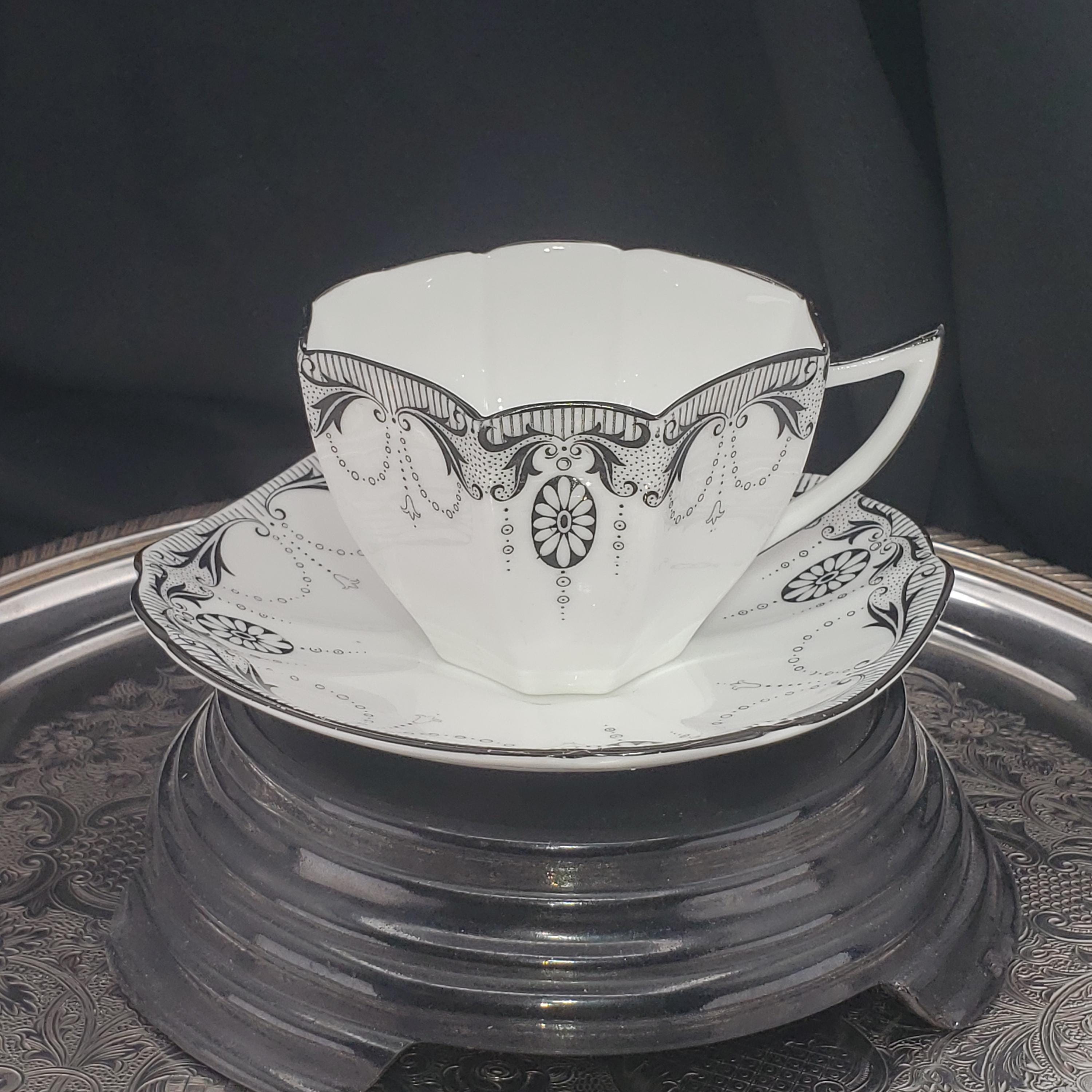 A white teacup with an ornate black and white design sits on a silver tray against a dark background.