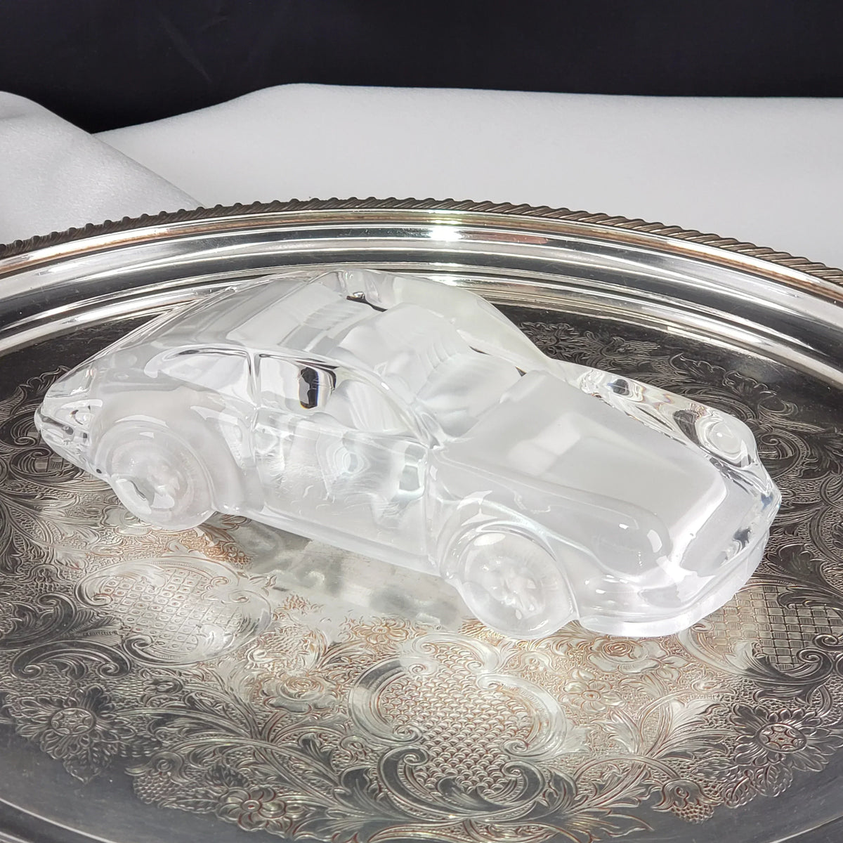 Clear glass vintage car figurine on a decorative silver tray.