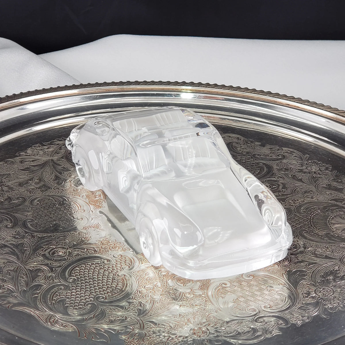 Vintage clear glass car figurine displayed on an ornate silver tray.