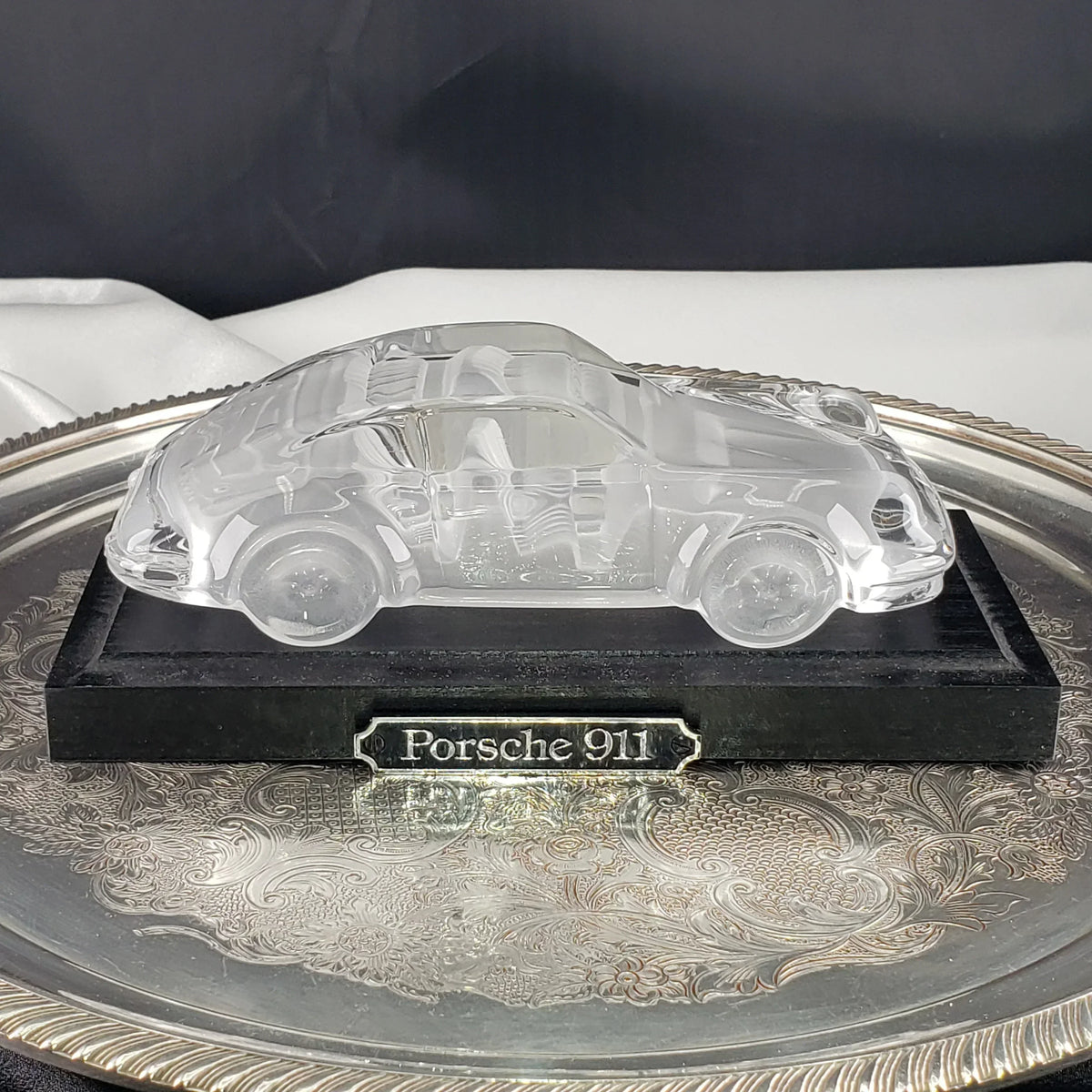 Clear crystal Porsche 911 car figurine on a black base and silver tray.