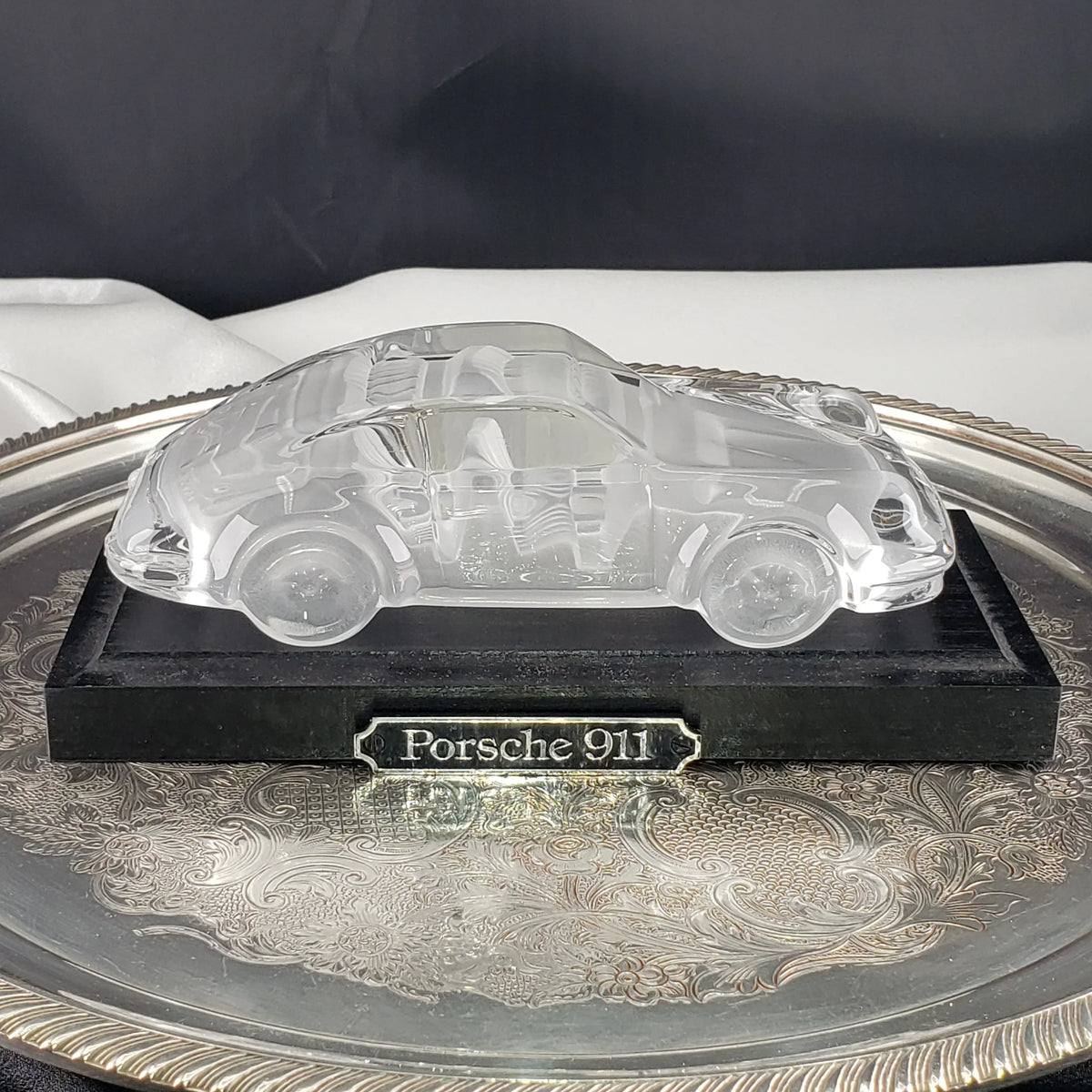 Clear crystal Porsche 911 car figurine on a black base and silver tray.
