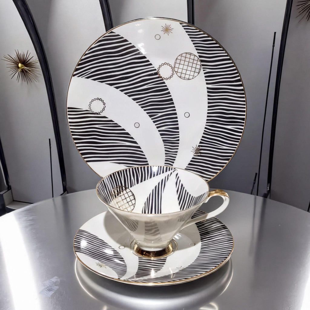 a white teacup and saucer with a black and white striped pattern, placed on a silver table.