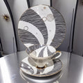a white teacup and saucer with a black and white striped pattern, placed on a silver table.