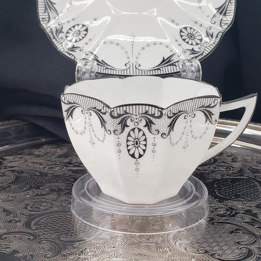 A white teacup with black floral designs on a tray, placed on a patterned surface.