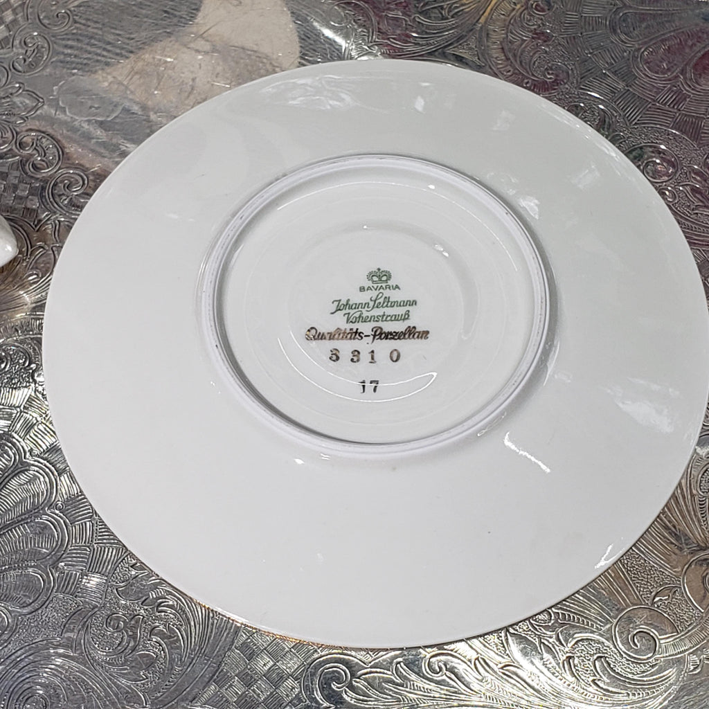 A white porcelain plate with a gold rim, featuring a floral pattern and text that reads "John Jettmann, Quattro Stemmed".