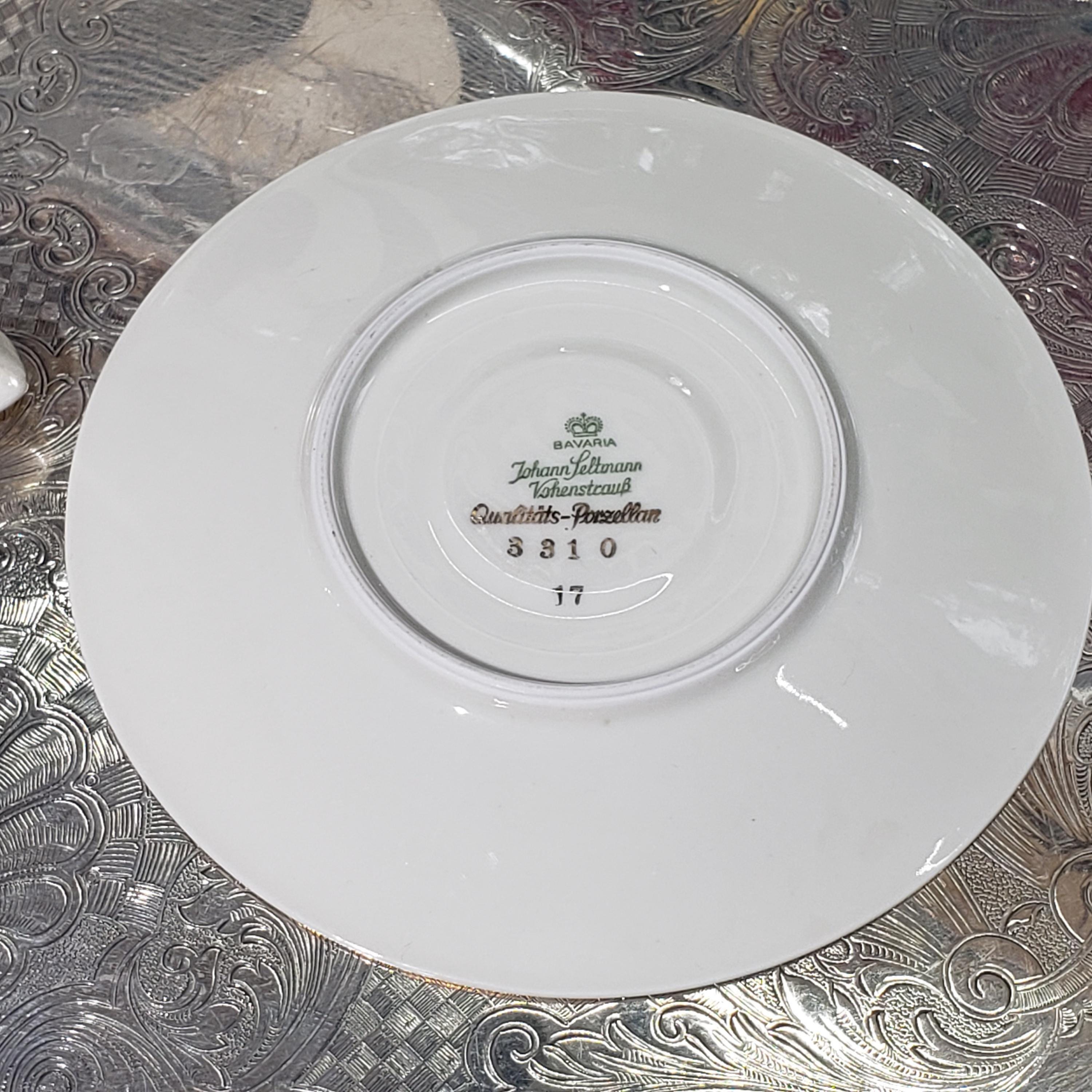 A white porcelain plate with a gold rim, featuring a floral pattern and text that reads "John Jettmann, Quattro Stemmed".
