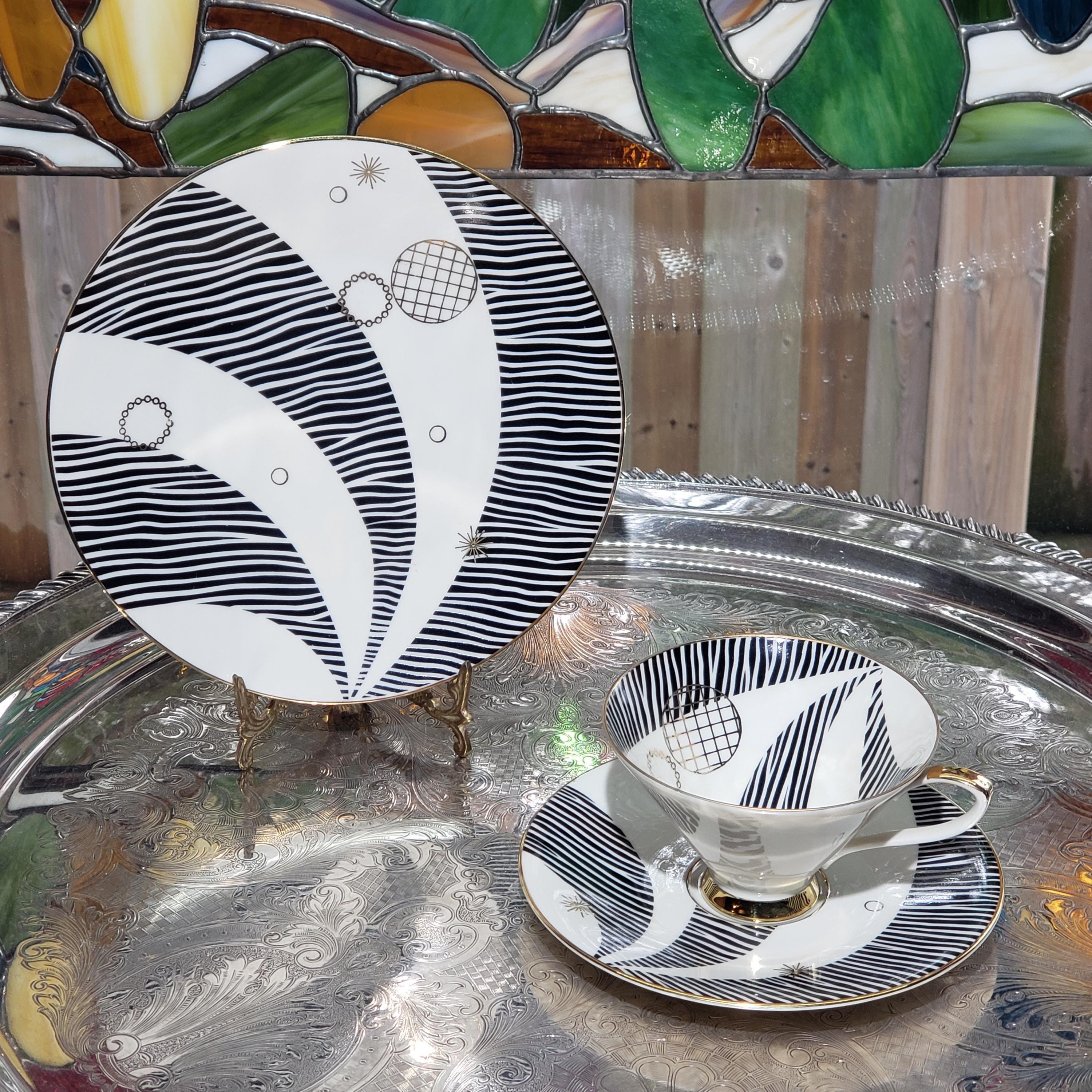 a decorative plate and a matching teacup, both with black and white striped designs, placed on a reflective surface.