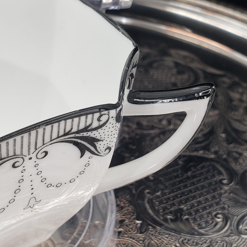A close-up view of a white ceramic mug with a black and white floral design on its side, resting on a metal tray.