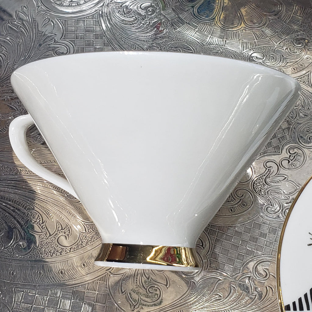 A white ceramic mug with a gold rim is placed on a patterned surface.