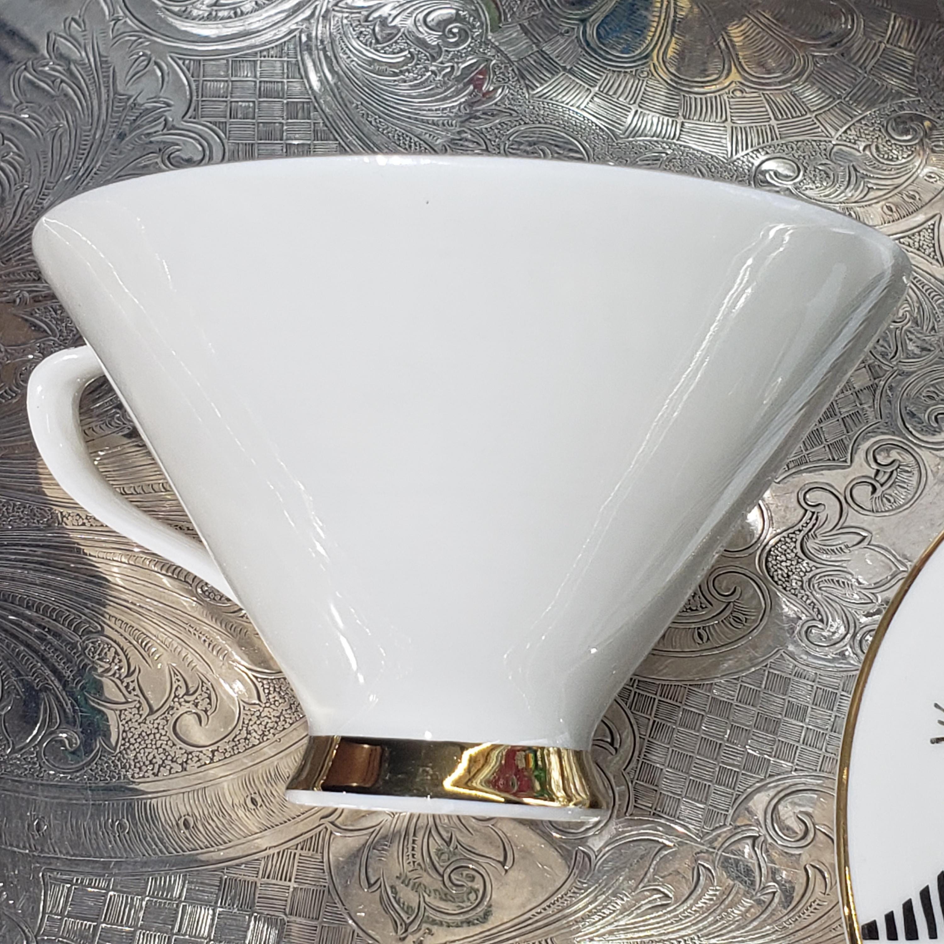 A white ceramic mug with a gold rim is placed on a patterned surface.