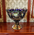 a large, ornate glass bowl with a colorful, iridescent design. The bowl is placed on a white pedestal, which is positioned on a white platform in an indoor setting.