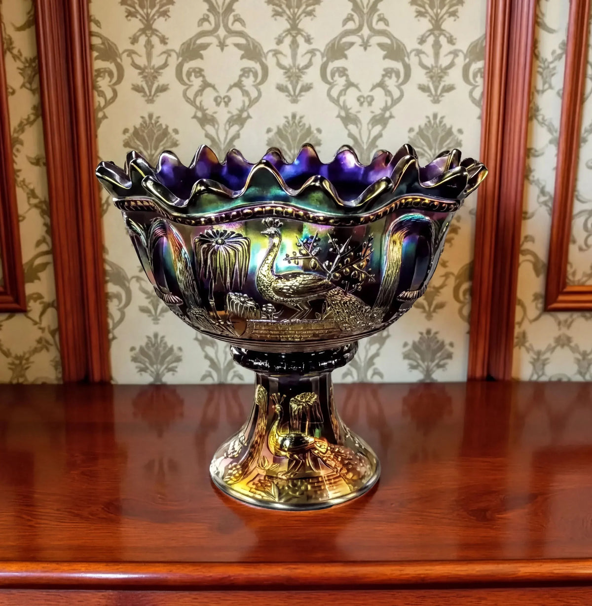 a large, ornate glass bowl with a colorful, iridescent design. The bowl is placed on a white pedestal, which is positioned on a white platform in an indoor setting.