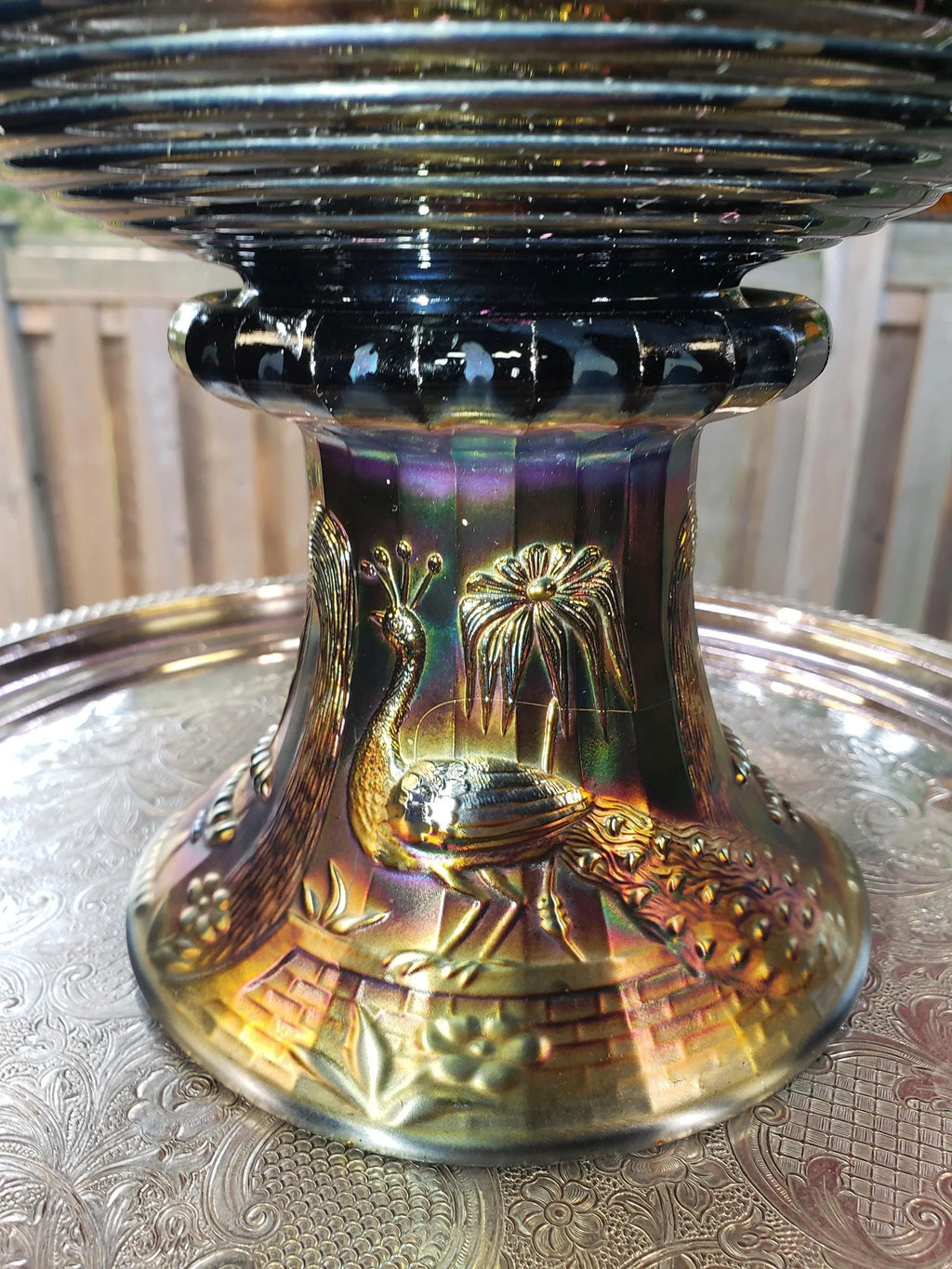 a decorative metal vase with a peacock design, sitting on a metal tray.