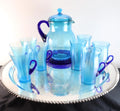 Light blue iridescent Fenton Glass pitcher with two different styles of 4 glasses. Celeste Pattern from the 1920s