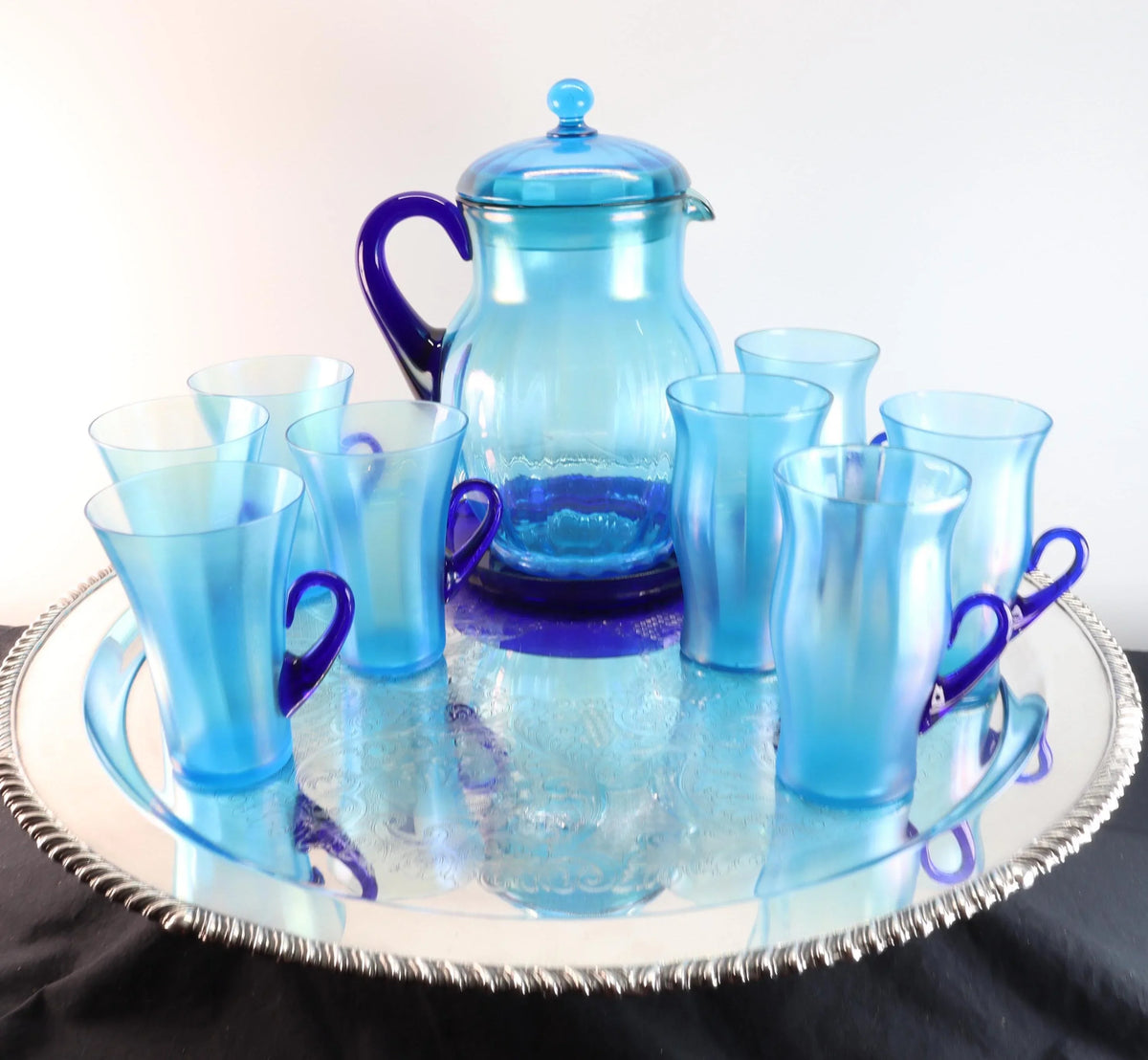 Light blue iridescent Fenton Glass pitcher with two different styles of 4 glasses. Celeste Pattern from the 1920s