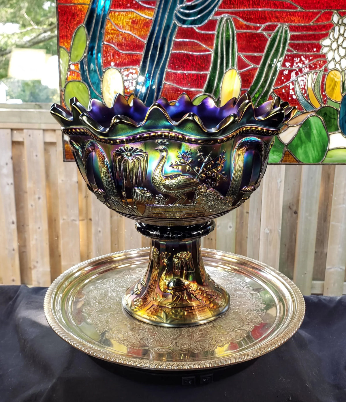a decorative bowl with a bird design, placed on a metal tray. The bowl is surrounded by a colorful, stained glass-like background, creating a visually appealing and artistic display.