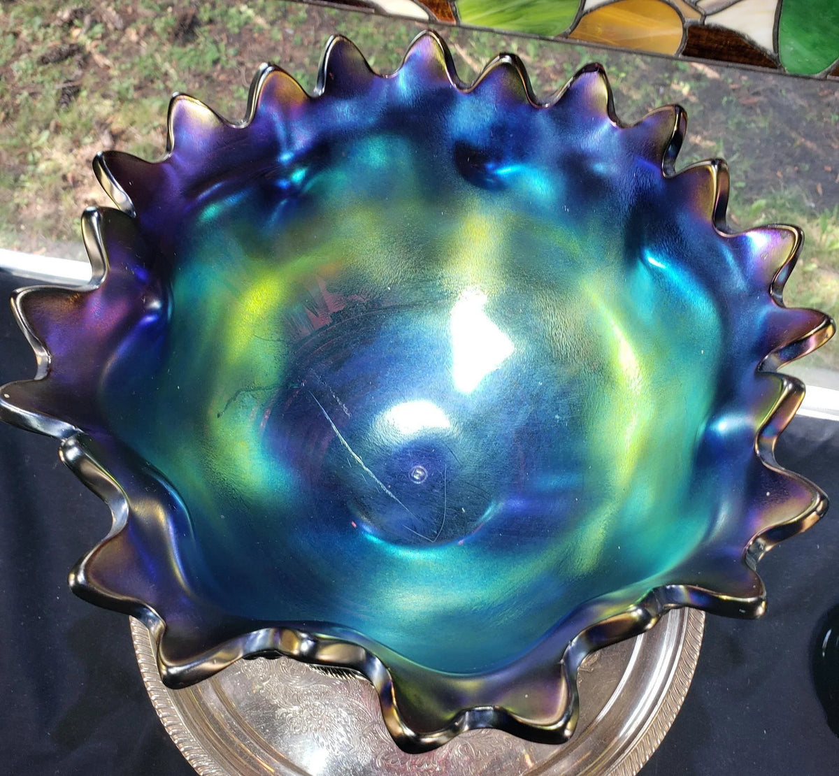 a large, colorful glass bowl with a blue and green iridescent surface, sitting on a metal stand.