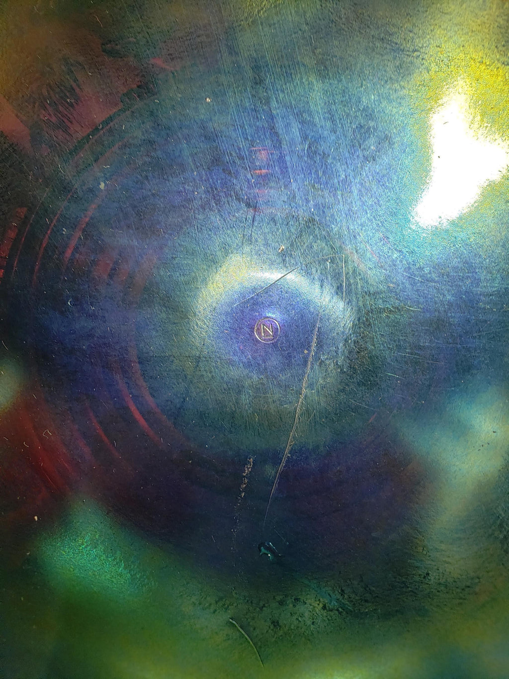 The image is a close-up of a metal surface with a spiral pattern, featuring a small circular object in the center.
