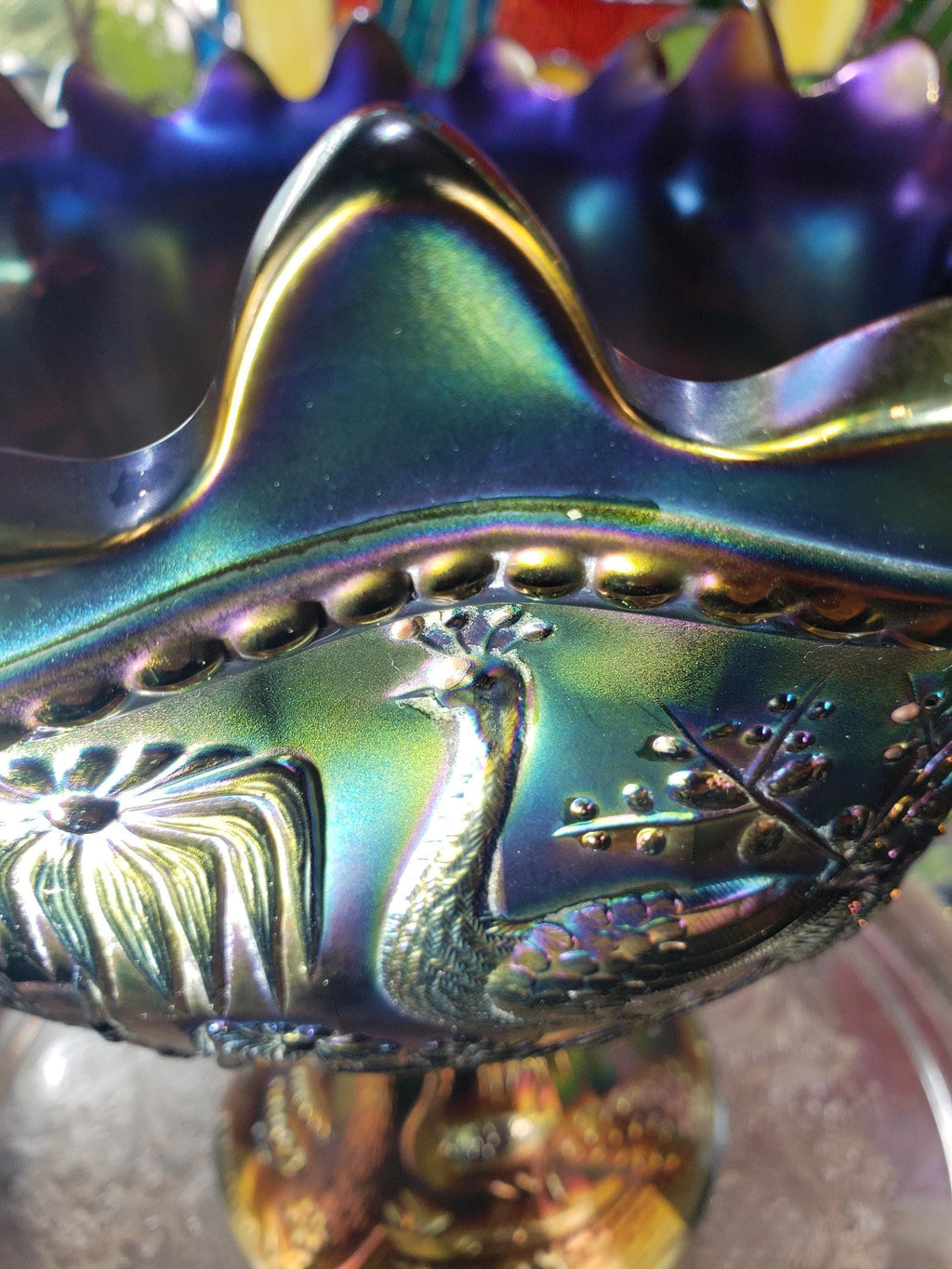 A close-up image of a decorative glass bowl with a peacock design, featuring a vibrant blue and green color scheme.